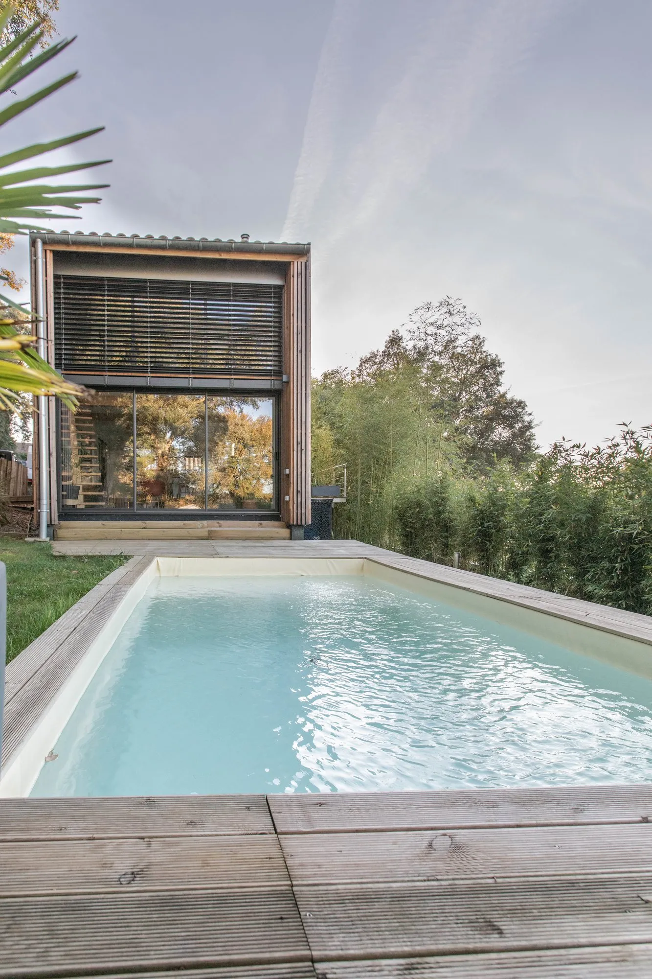 La piscine bordée de lames de bois, la maison au fond